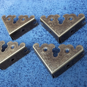 May include: Four antique gold corner brackets with a decorative floral design. The brackets are made of metal and have a distressed finish.
