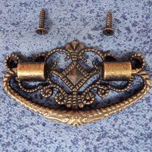 Peut inclure: Une poignée de tiroir décorative en métal doré orné avec un centre en forme de diamant et deux vis.