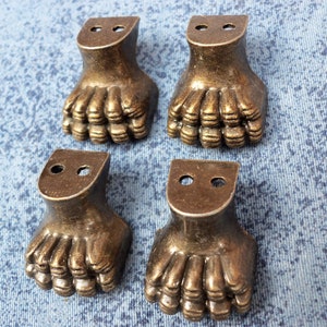 Op de afbeelding: Vier antieke goudkleurige meubelpoten met een klauwontwerp. Elke poot heeft twee gaten aan de bovenkant.