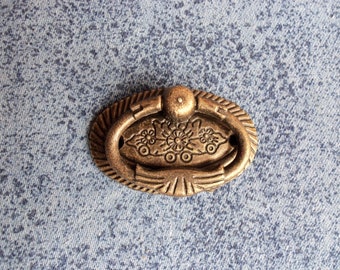 Könnte beinhalten: Ein ovaler Schrankgriff in Goldton mit einem dekorativen Blumendesign und einem Ringgriff.