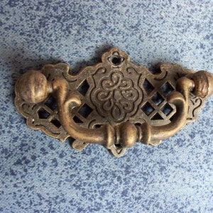 Può includere: Una maniglia per cassetto decorativa in ottone con un design a traliccio e dettagli decorativi. La maniglia ha due pomelli rotondi su ciascuna estremità.