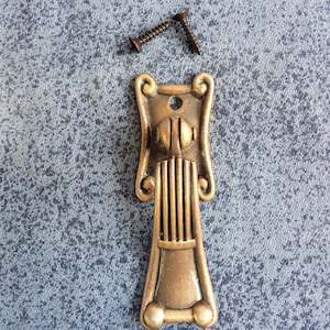 May include: A gold-toned metal cabinet door pull with an ornate design. The pull has a round knob and a vertical fluted section. Two screws are included.