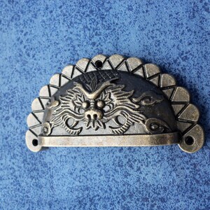 May include: A half-round, antique-style drawer pull with a dragon design. The pull is made of metal and has a dark bronze finish.