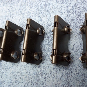 Puede incluir: Cuatro soportes de esquina de metal negro con agujeros para tornillos y una bisagra. Los soportes están diseñados para usarse para unir dos piezas de madera u otros materiales en un ángulo de 90 grados.