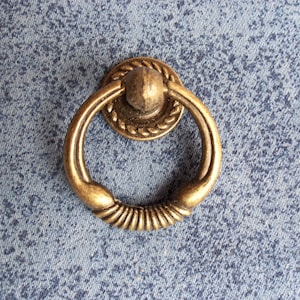 Puede incluir: Una manija de puerta de armario de anillo de color dorado con un diseño de cuerda decorativo.