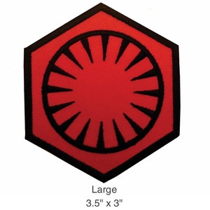 Puede incluir: Un parche hexagonal rojo y negro con un símbolo estilizado de un círculo con líneas radiantes. El parche mide 3,5 pulgadas por 3 pulgadas y está etiquetado como "Large".