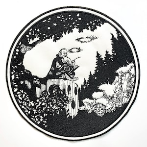 Puede incluir: Parche bordado en blanco y negro que representa a un hombre con barba sentado en un borde, mirando hacia arriba a un halo en el cielo. El hombre sostiene un libro y hay árboles en el fondo.