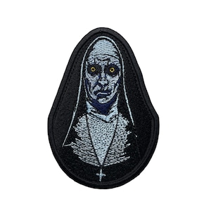 Peut inclure: Patch brodé noir représentant une religieuse avec une robe blanche et une croix. La religieuse a un visage pâle avec des yeux sombres et une expression sérieuse.