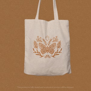 May include: A white tote bag with a brown butterfly and floral design. The design includes acorns, leaves, and mushrooms.