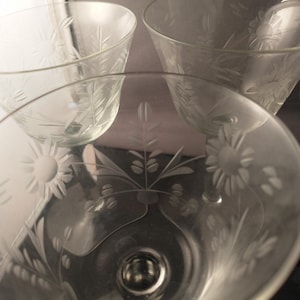 May include: Three clear glass drinking glasses with an etched floral design. The glasses are stacked on top of each other.