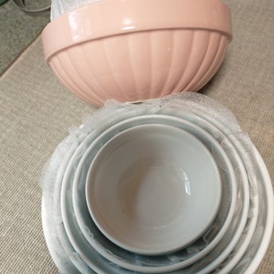 May include: A set of nesting bowls, one pink and four white. The bowls are stacked inside each other, with the pink bowl on top.
