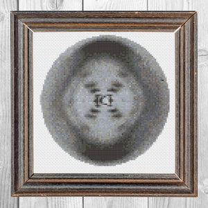 May include: A square dark brown wooden frame containing a circular cross-stitch embroidery piece. The embroidery features a pixelated, abstract pattern in shades of gray, blue, and black, centered on a white fabric background with a visible grid.