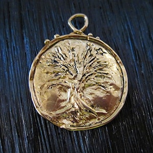 May include: A gold pendant featuring a detailed embossed tree design. The pendant is round and has a textured surface.