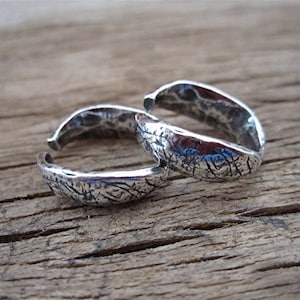 May include: Two silver toe rings with a textured hammered finish. The rings are open and adjustable.