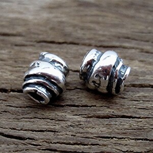 May include: Two silver beads with a textured, twisted design. The beads are made of metal and have a shiny finish.