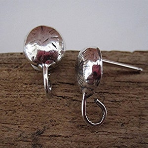 May include: A pair of silver-colored earrings with a hammered texture. Each earring has a rounded, domed shape with a small hook. The earrings are displayed on a wooden surface.