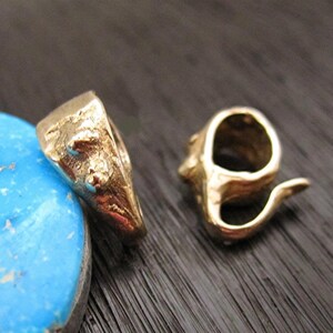 May include: Two small, gold-colored metal rings. One ring has a textured surface with small turquoise accents. The other ring has a spiral design. The rings are displayed on a dark surface.