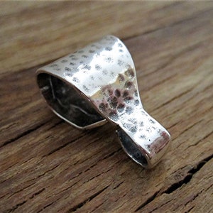 May include: A silver pendant with a hammered texture. The pendant has a loop at the top for attaching to a chain or cord.