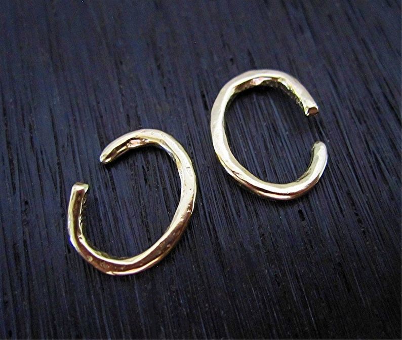 May include: Two gold-toned ear cuffs, each shaped like a simple, slightly irregular circle. The cuffs are made of a hammered metal, giving them a textured surface.