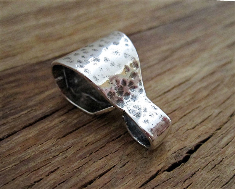 May include: A silver pendant with a hammered texture. The pendant has a loop at the top for attaching to a chain or cord.