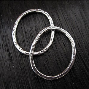 May include: Two silver rings with a hammered texture, intertwined and laying on a black surface.