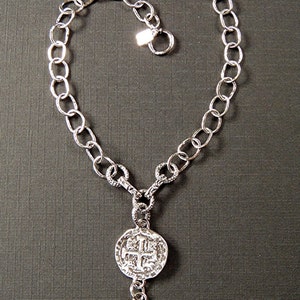 May include: A silver chain necklace with two silver coin pendants. The coins have a cross design.