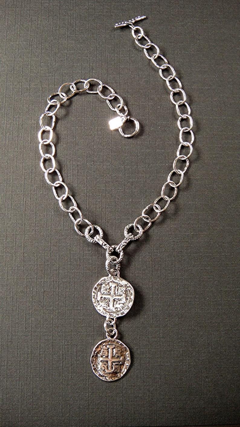 May include: A silver chain necklace with two silver coin pendants. The coins have a cross design.