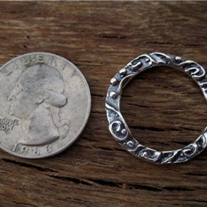 May include: A silver ring with a textured, ornate design. The ring is shown next to a US quarter for size comparison.