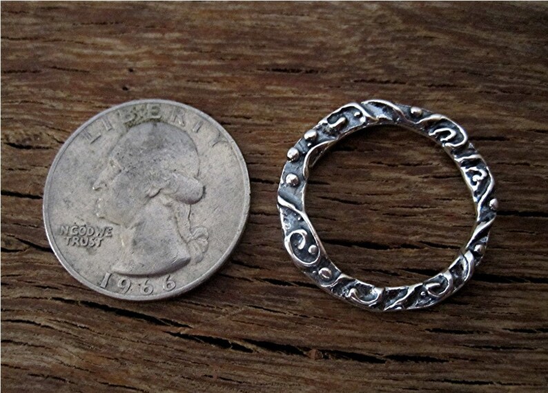 May include: A silver ring with a textured, ornate design. The ring is shown next to a US quarter for size comparison.