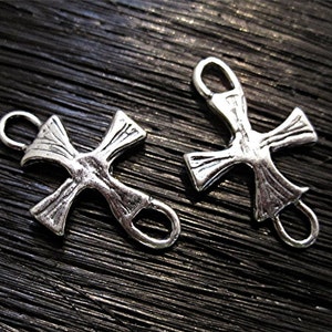 May include: Two silver-toned cross charms with a decorative design. Each charm has a loop at the top and a loop on the side for attaching to a chain or bracelet.