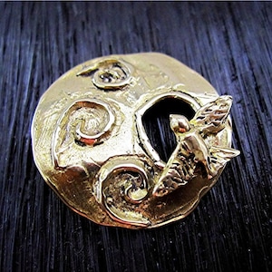 May include: A gold-toned metal pendant featuring a stylized bird in flight, with a textured background of swirling lines.