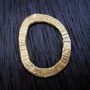 以下が含まれることがあります： 表面がテクスチャ加工された金色の金属製のリング。リングは円形で、内側の縁は滑らかです。