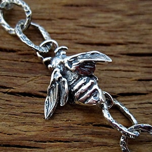 May include: A silver charm bracelet with a detailed bee charm. The bracelet has a textured chain and the bee charm has a textured body and wings.