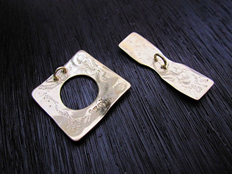 May include: Two gold-toned metal buttons with a textured surface. One button is square with a round hole in the center. The other button is a long oval shape.