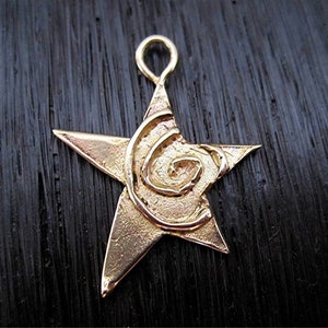 May include: A gold-toned star-shaped pendant with a spiral design in the center. The pendant has a loop at the top for attaching to a chain.
