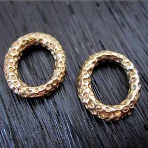 May include: Two gold-colored metal rings with a textured surface. The rings are round and have a smooth inner edge.