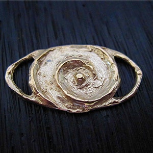 May include: A gold-toned metal toggle clasp with a spiral design. The clasp has a textured surface and a smooth, round center.