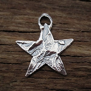May include: A silver star charm with a textured surface. The charm has a loop at the top for attaching to a necklace or bracelet.