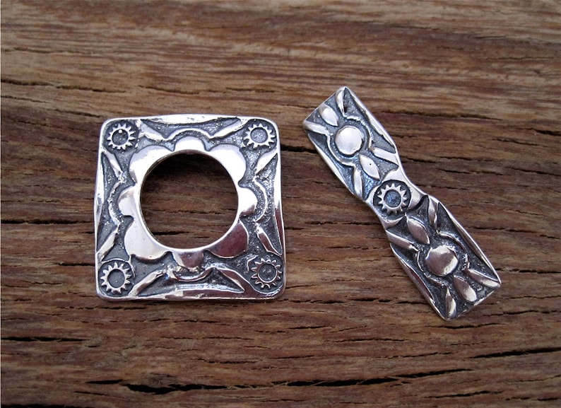 May include: Two silver metal decorative pieces with intricate floral designs. The piece on the left is square with a circular opening in the center. The piece on the right is a long, narrow rectangle.