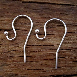 May include: Two silver-colored earring hooks with a rounded top and a small ball at the end of the hook. The hooks are displayed against a brown wooden background.