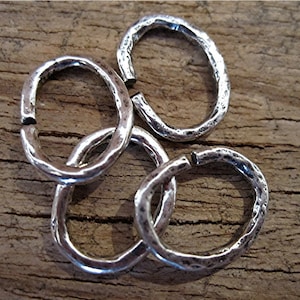 May include: Four silver jump rings with a hammered texture. The rings are oval shaped and are approximately 1 inch in diameter.