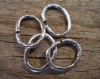 May include: Four silver-coloured, hammered-look oval rings. The rings are interlocked and have a textured surface. The background is a weathered wooden surface. These rings could be used for jewellery making or other craft projects.