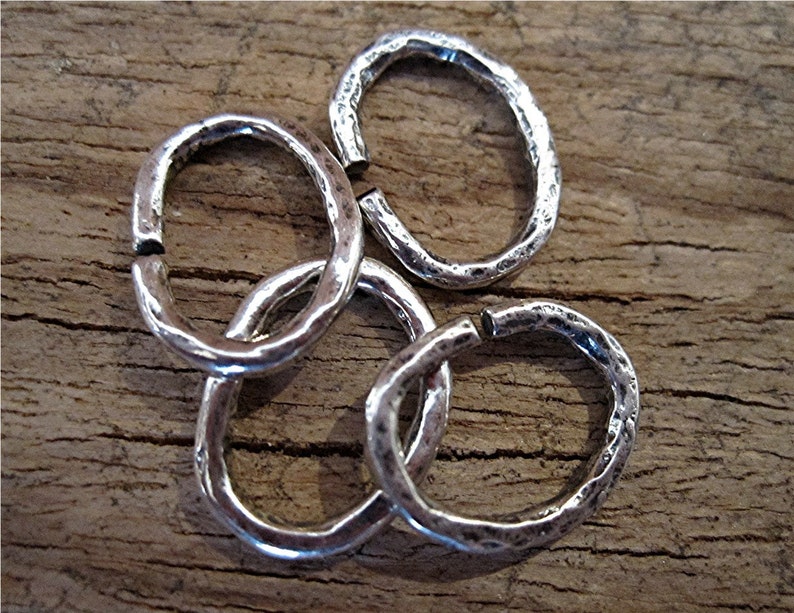May include: Four silver jump rings with a hammered texture. The rings are oval shaped and are approximately 1 inch in diameter.