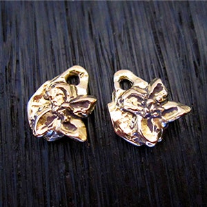 May include: Two gold-colored metal charms shaped like stylized butterflies with a hole at the top for attaching to a chain or bracelet.