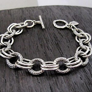 May include: A silver chain bracelet with a textured finish. The bracelet has a t-bar clasp.