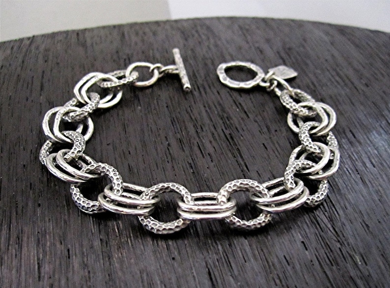 May include: A silver chain bracelet with a textured finish. The bracelet has a t-bar clasp.