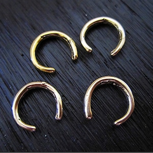 Puede incluir: Cuatro pendientes de aro de color dorado, cada uno con forma de semicírculo, están dispuestos sobre una superficie de madera oscura.