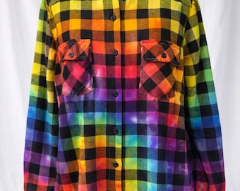 May include: Rainbow plaid button-down shirt with two chest pockets. The shirt features a vibrant gradient of colors, including yellow, orange, red, purple, and blue, transitioning into a black and white checkered pattern. The long-sleeved shirt is displayed on a white mannequin.