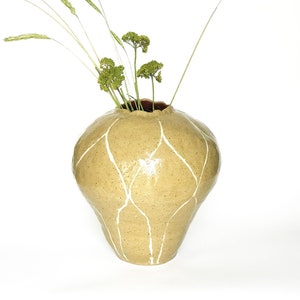 May include: A light yellow ceramic vase with a white geometric design. The vase is filled with dried grasses and flowers.