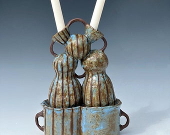 May include: A ceramic candle holder with two white candles. The holder is decorated with brown and blue stripes and has a textured surface.